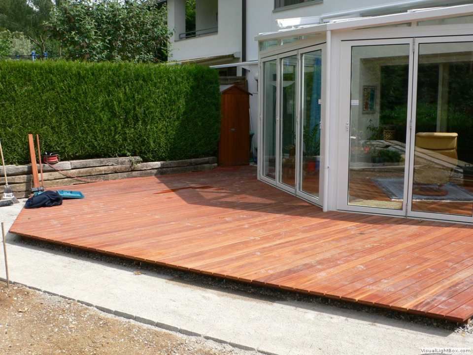 Eine Holzterrasse vor einem Haus mit Glasschiebetüren