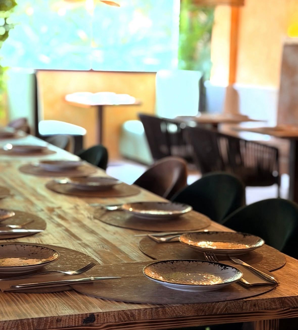 Mesa de comedor iluminada por el sol, con platos y vasos, en un restaurante moderno o en un espacio al aire libre.