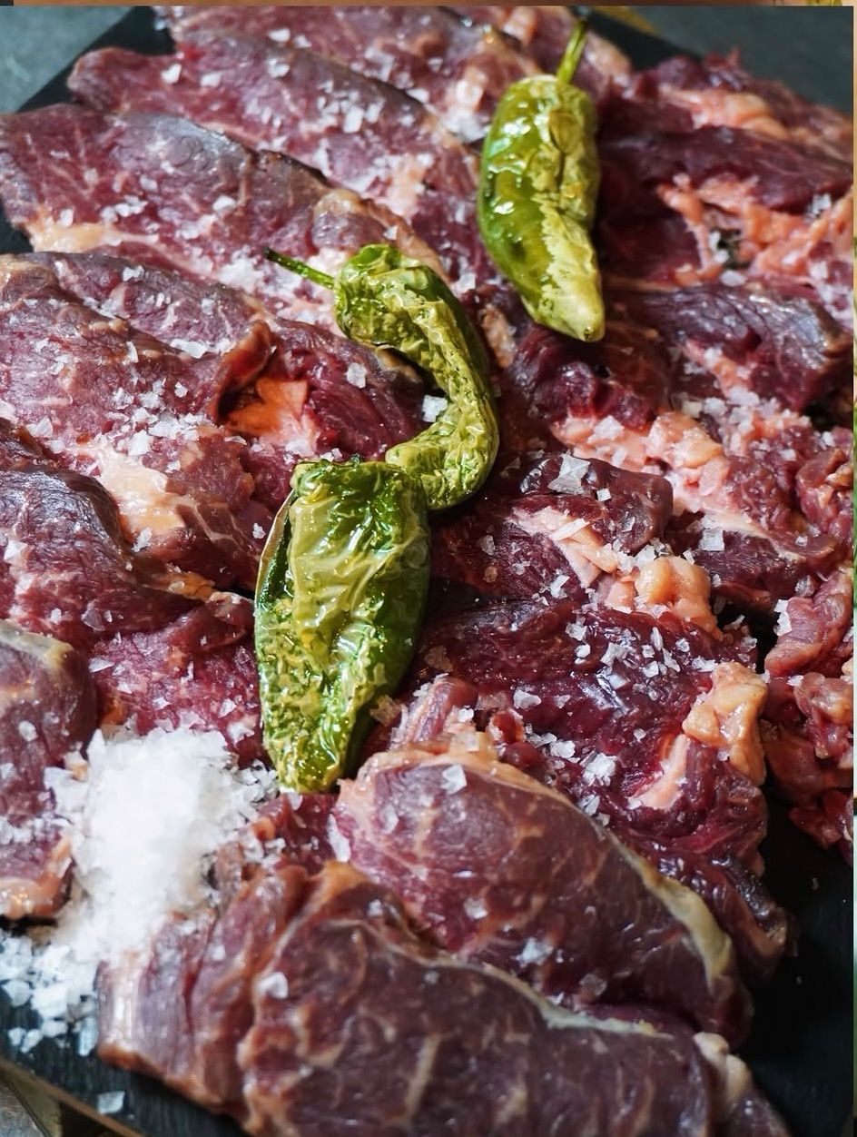 Carne cruda con chiles verdes y sal gruesa en una bandeja oscura.