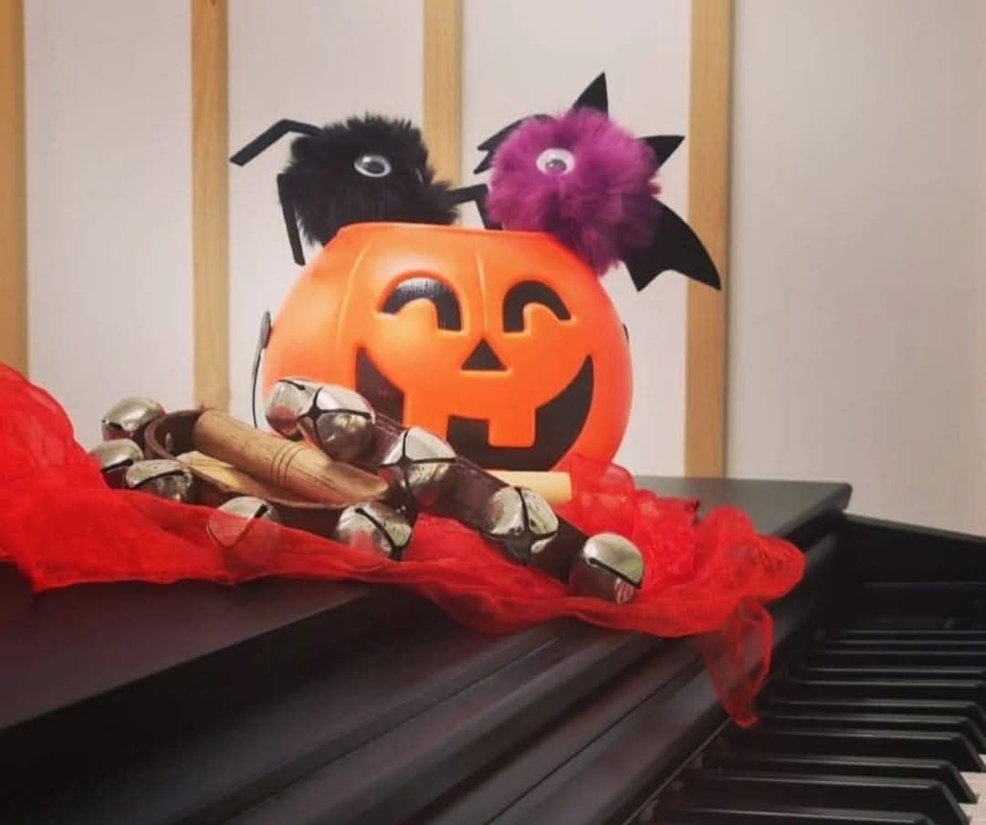 Decoración de calabaza de Halloween con murciélagos negros y morados de peluche sobre un piano, adornada con tul rojo.
