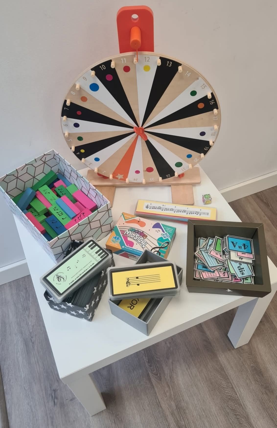 Una rueda de premios y varias cajas de regalo coloridas se exhiben sobre una pequeña mesa blanca en una habitación.