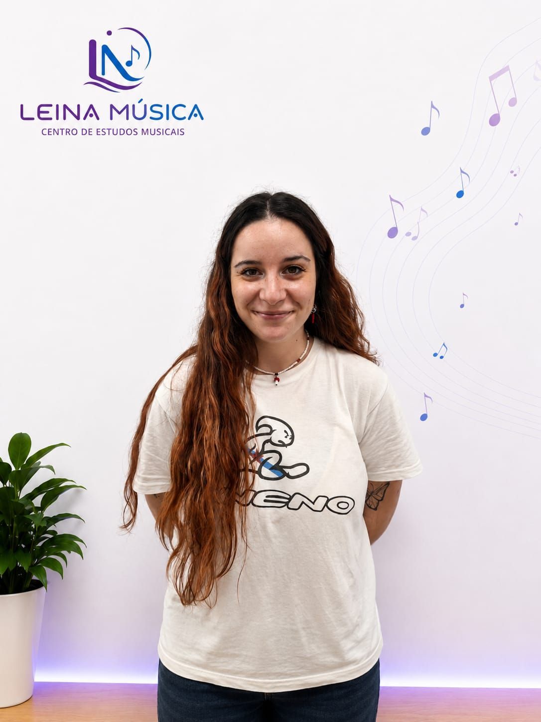 Mujer de pie en un estudio de música, con una camiseta blanca, y el logotipo de Leina Música en la pared.
