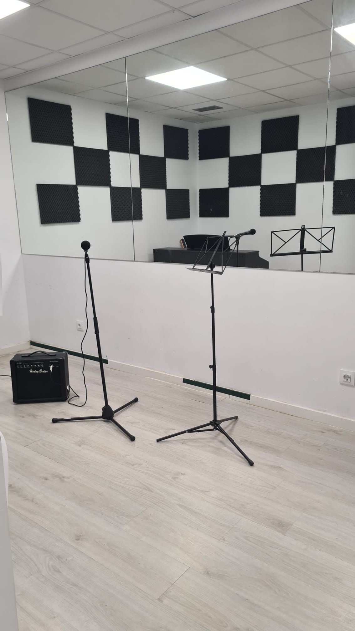 Estudio de grabación con paneles de pared insonorizados, dos soportes para micrófonos y un atril sobre un suelo blanco.
