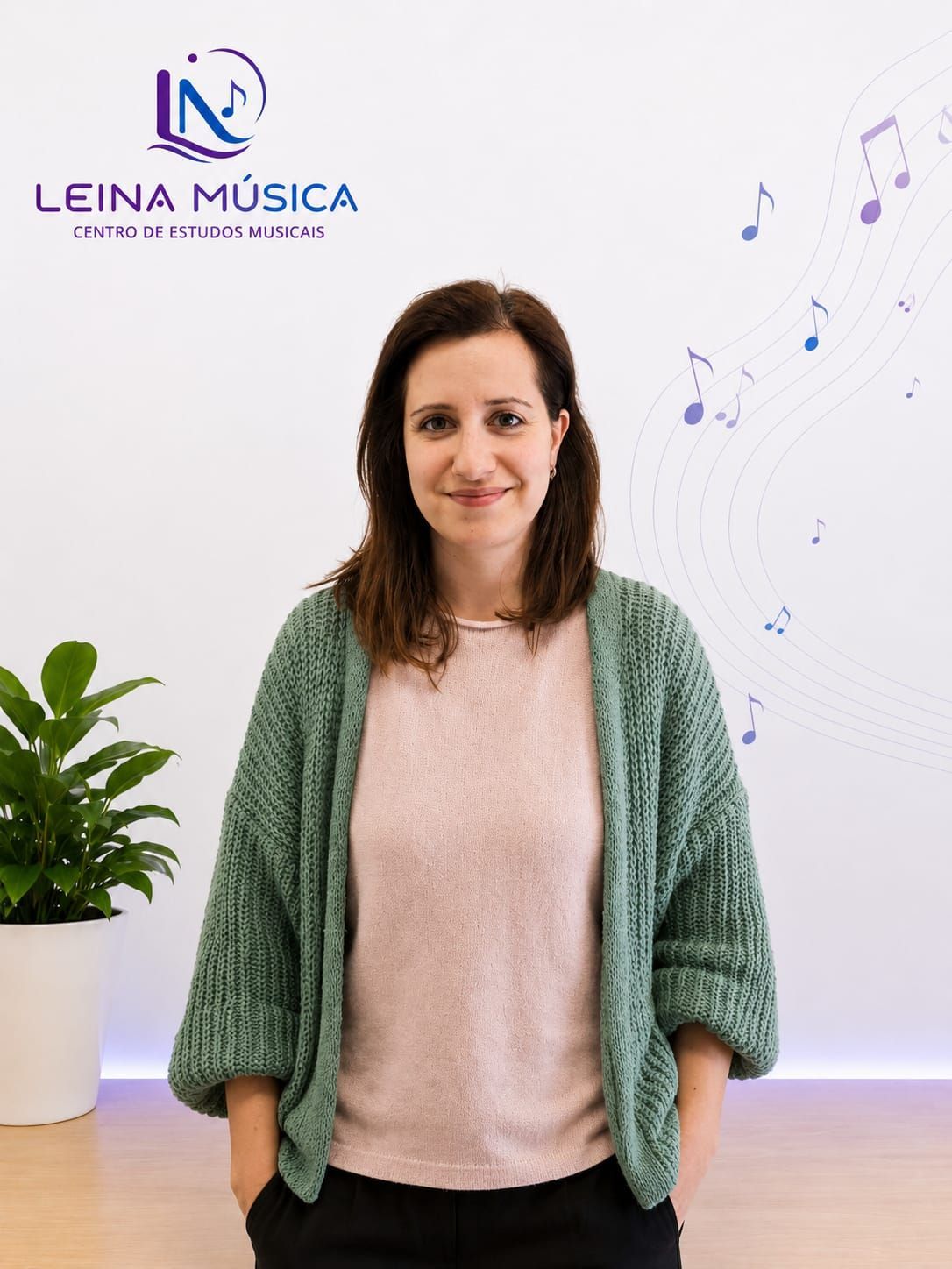 Mujer de pie en el interior de un edificio, frente al logo de León Música, con un cárdigan verde y sonriendo.
