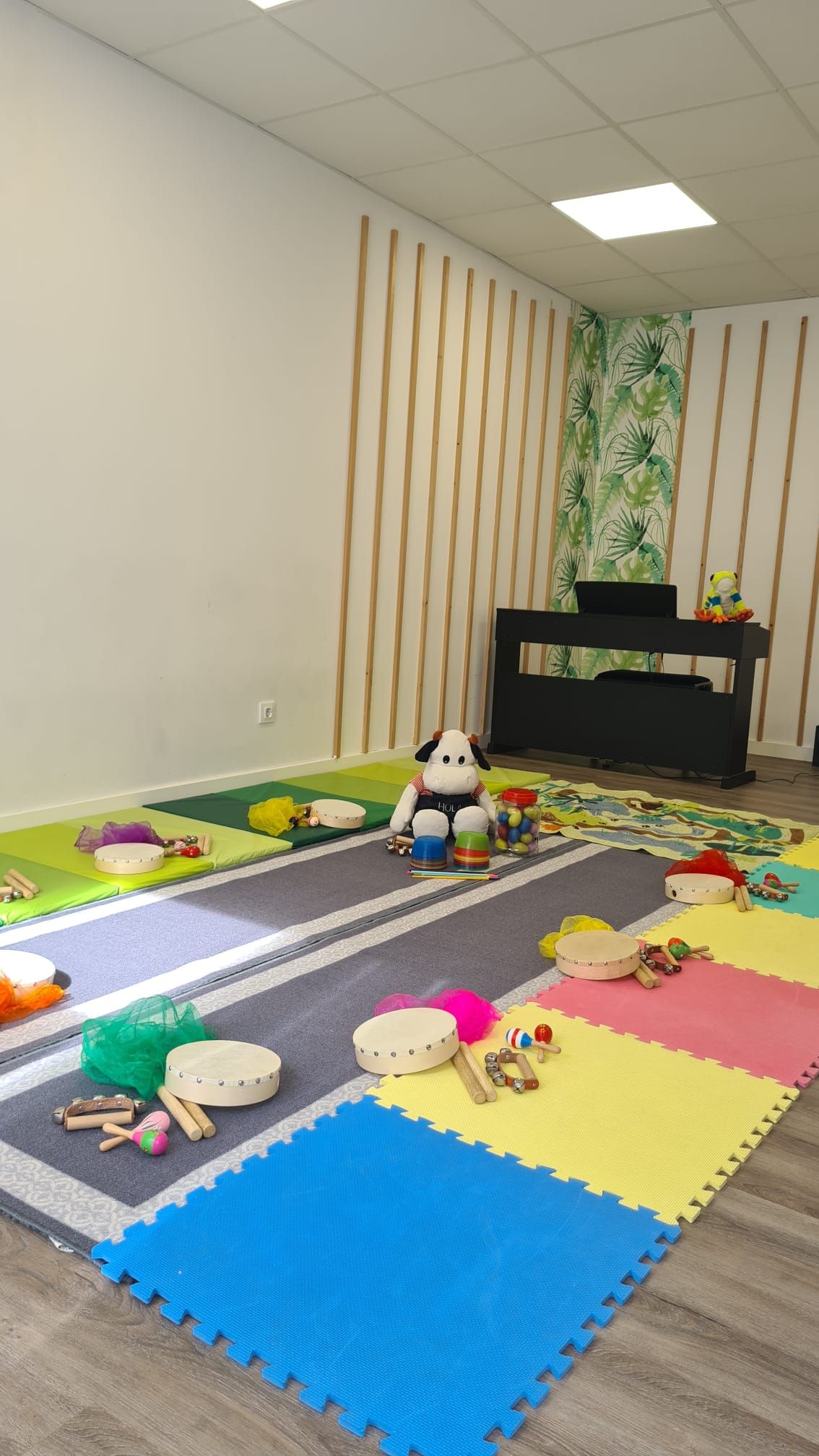 Alfombra de juegos de espuma colorida en una sala de juegos con juguetes de peluche y un piano en la esquina.