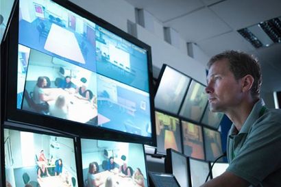 Un hombre está mirando un montón de monitores en una sala de control.