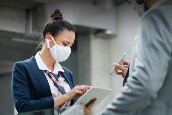 Una mujer que lleva una máscara usa una tableta mientras un hombre sostiene un teléfono celular.