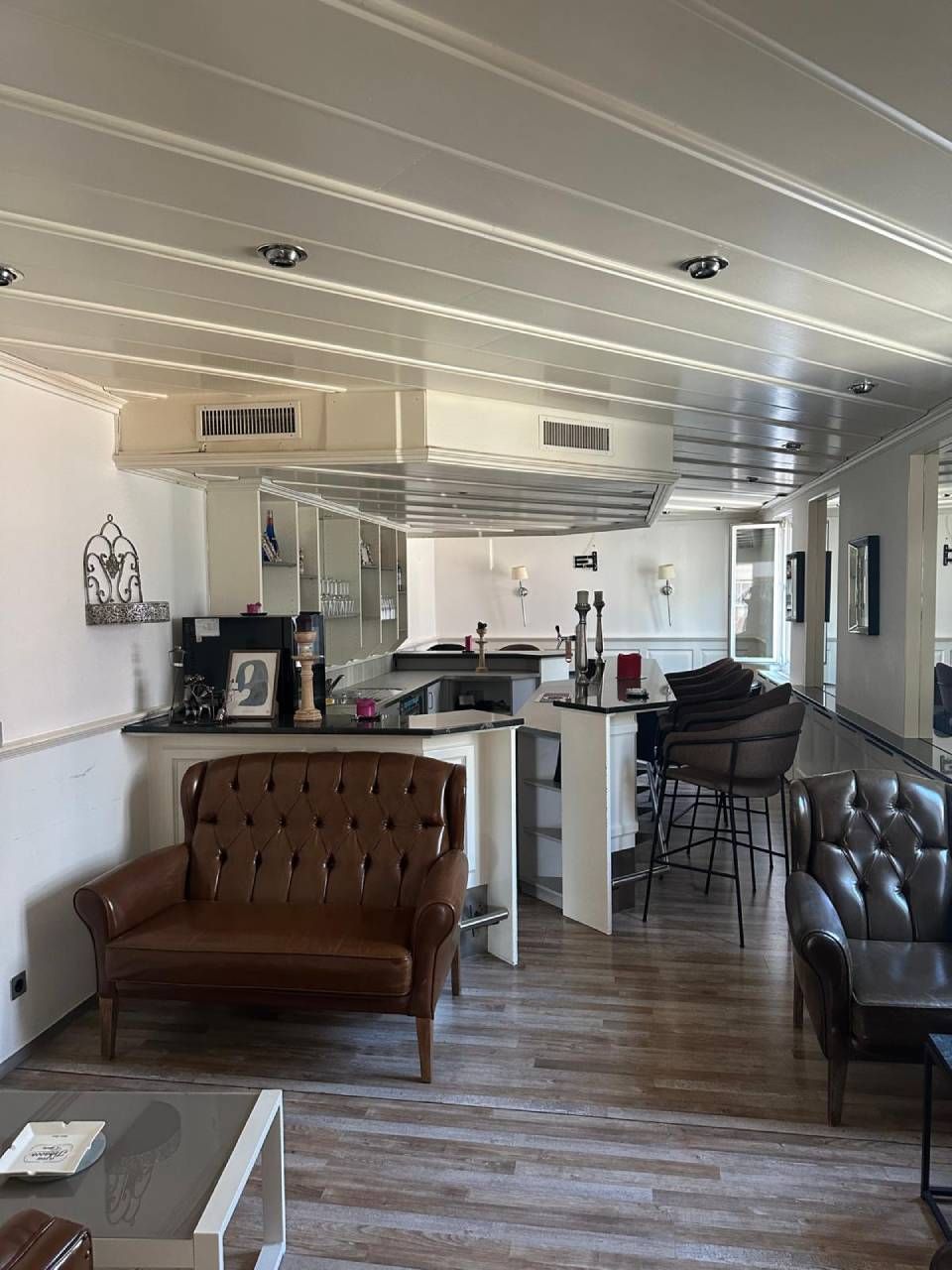Gemütliches Café-Interieur mit Ledersesseln, Holzboden, Theke und Pendelleuchten