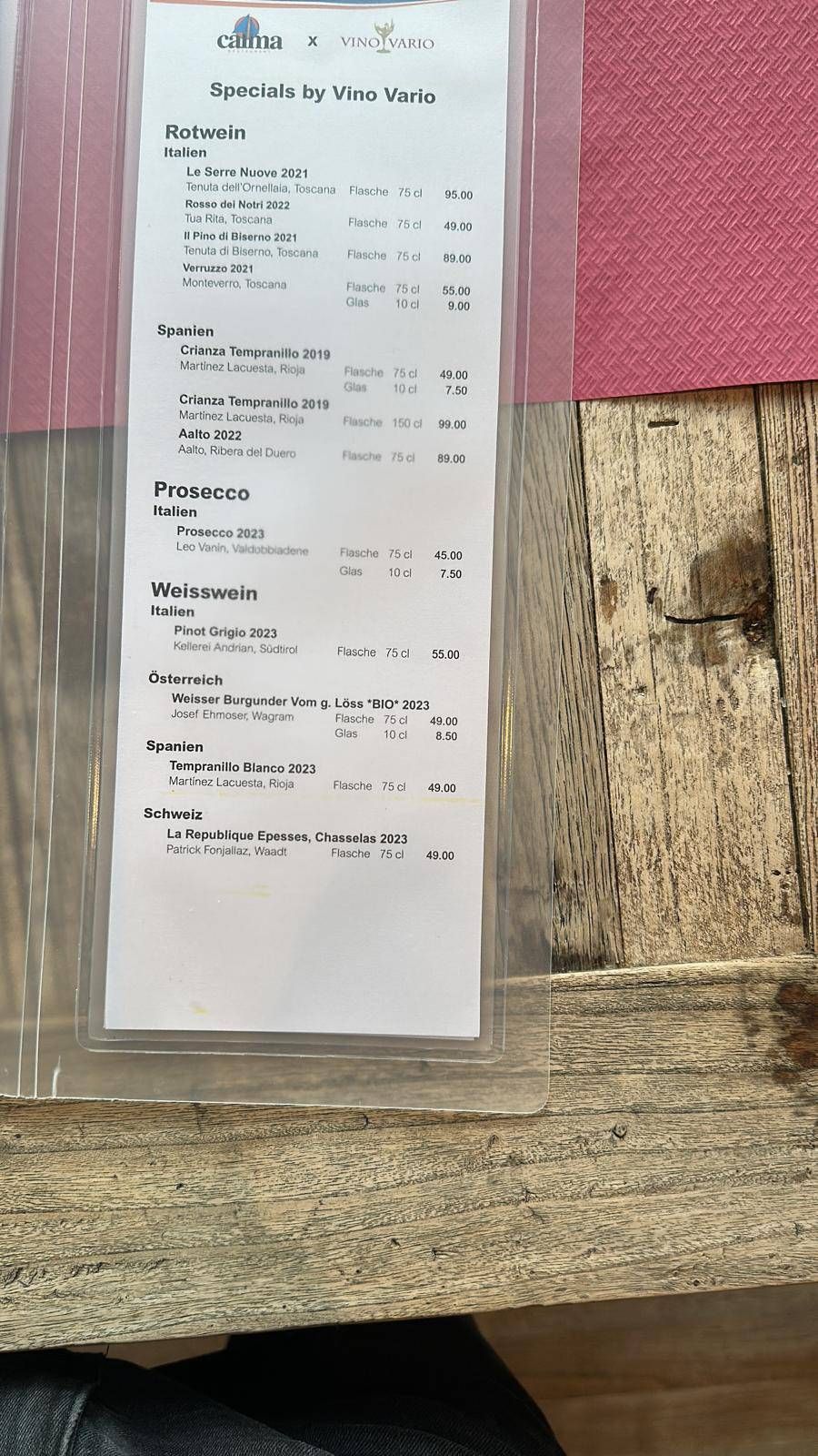 Ein langer Kassenbon klebt an einem verwitterten Holzbrett neben einer rosa Wand.