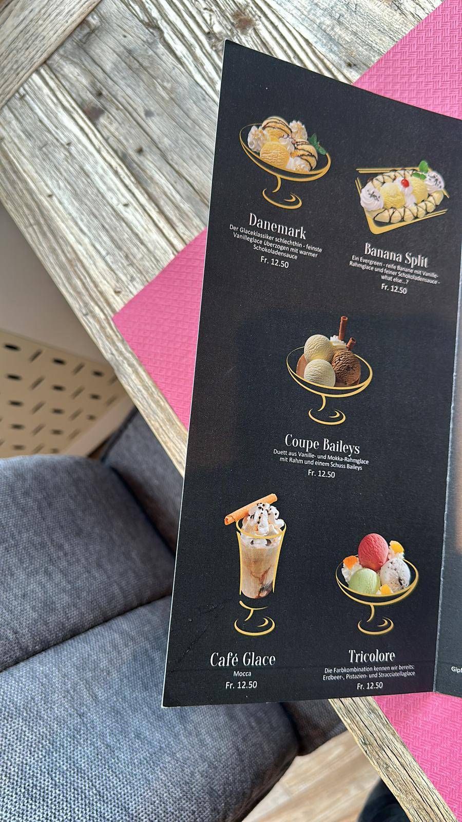 Schwarze Dessertkarte mit verschiedenen Eisbechern und Parfaits auf einer rosa gewebten Matte