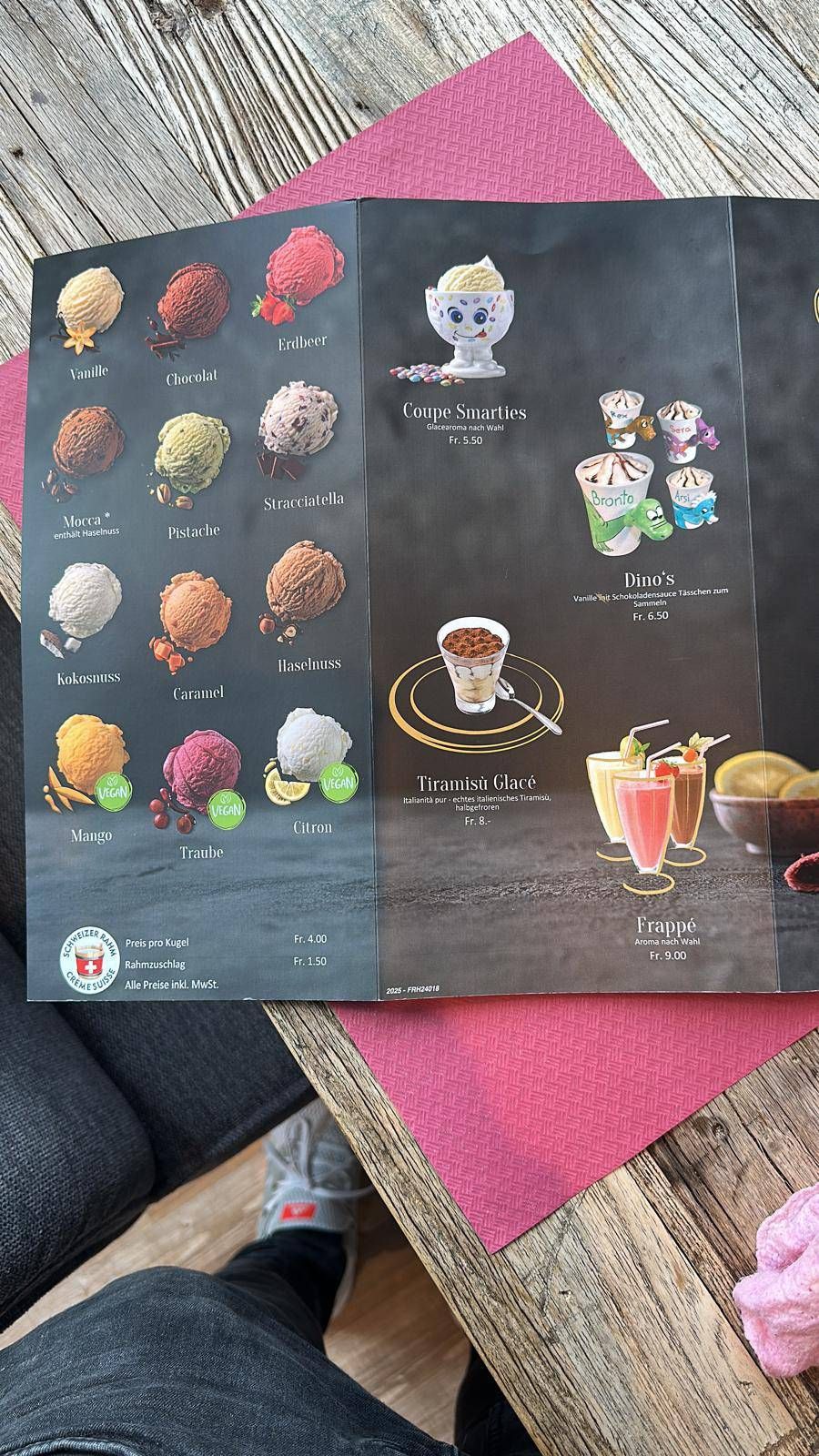 Speisekarte mit farbenfrohen Dessertillustrationen und Getränkefotos auf einem Tisch im Freien