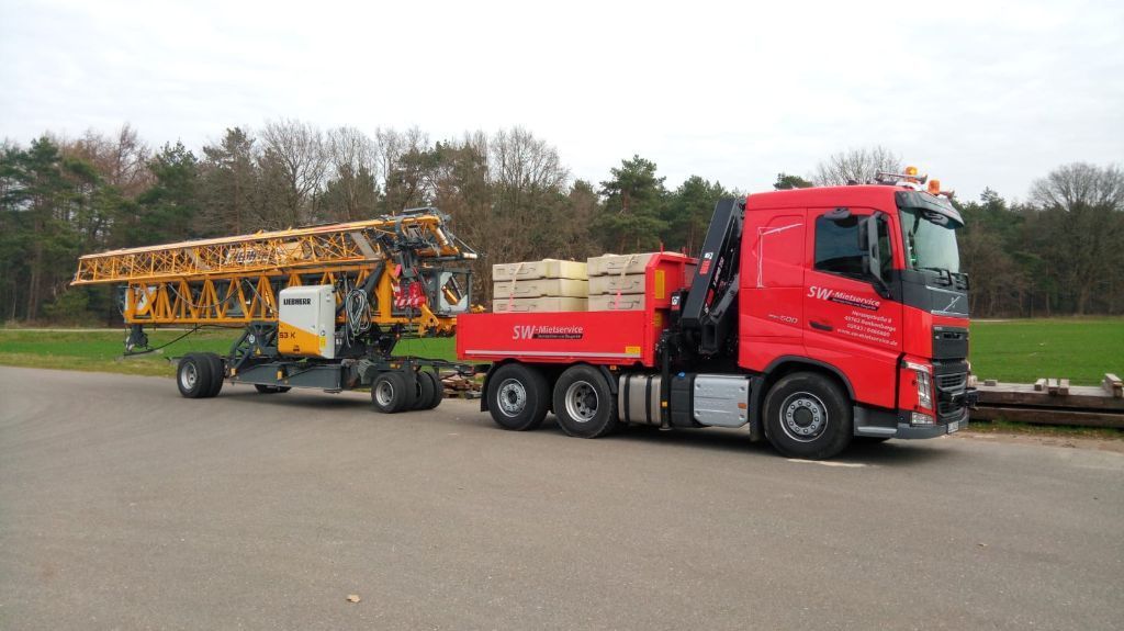 Ein roter Lastwagen schleppt einen gelben Kran eine Straße entlang.