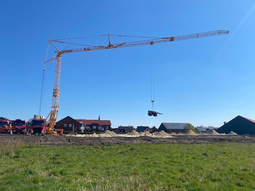 Ein Baukran hebt ein Stück Holz auf einem Feld an.