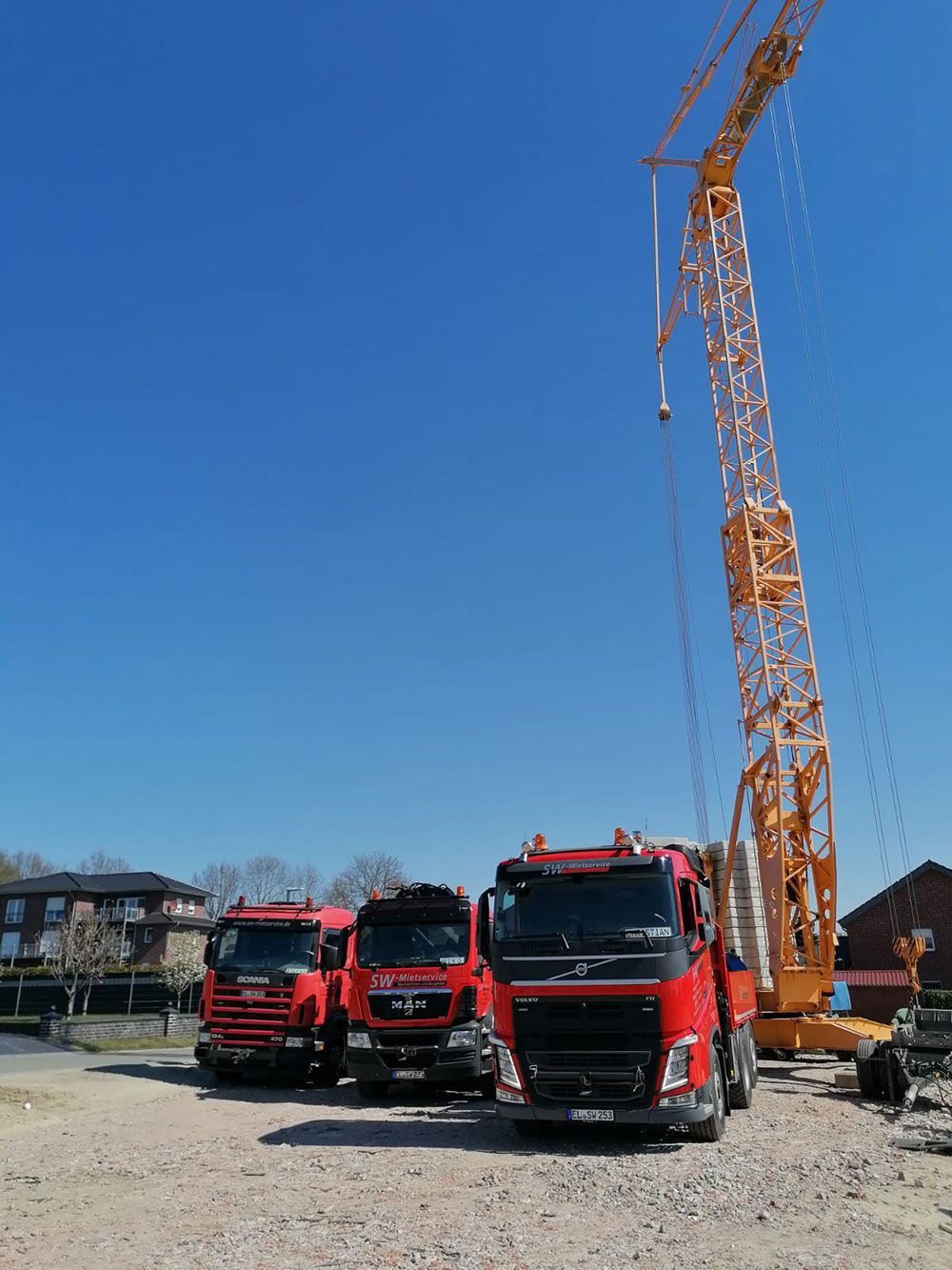 Eine Reihe roter Lastwagen parkt neben einem Kran