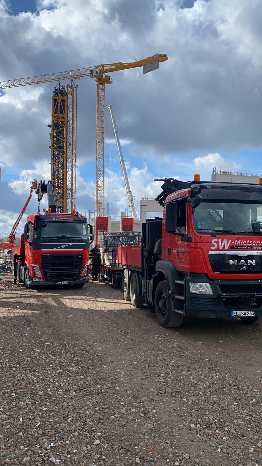 Zwei rote Lastwagen stehen nebeneinander auf einer Schotterstraße.