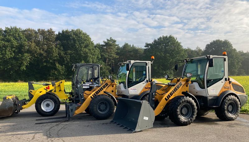 Drei Baufahrzeuge stehen nebeneinander am Straßenrand.