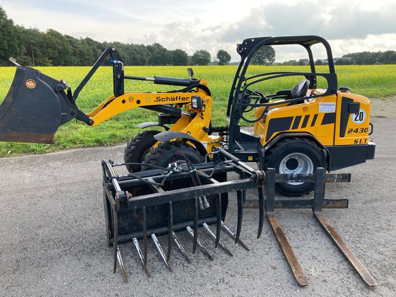 Am Straßenrand parkt ein gelber Gabelstapler mit einem daran befestigten Greifer.