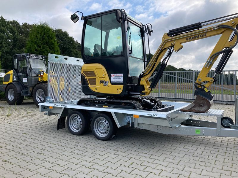 Auf einem Anhänger steht ein kleiner Bagger.