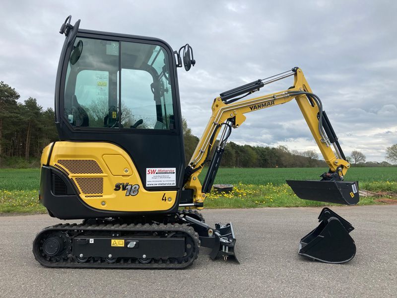 Am Straßenrand parkt ein kleiner gelb-schwarzer Bagger.