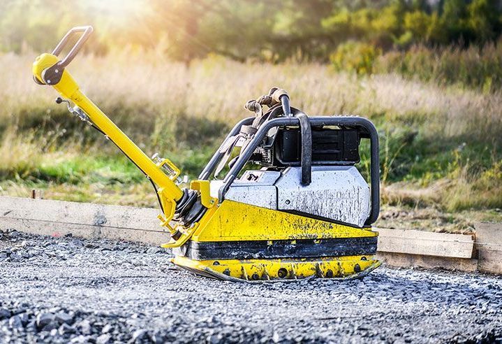 Auf einer Schotterstraße steht eine gelb-schwarze Müllverdichtermaschine.