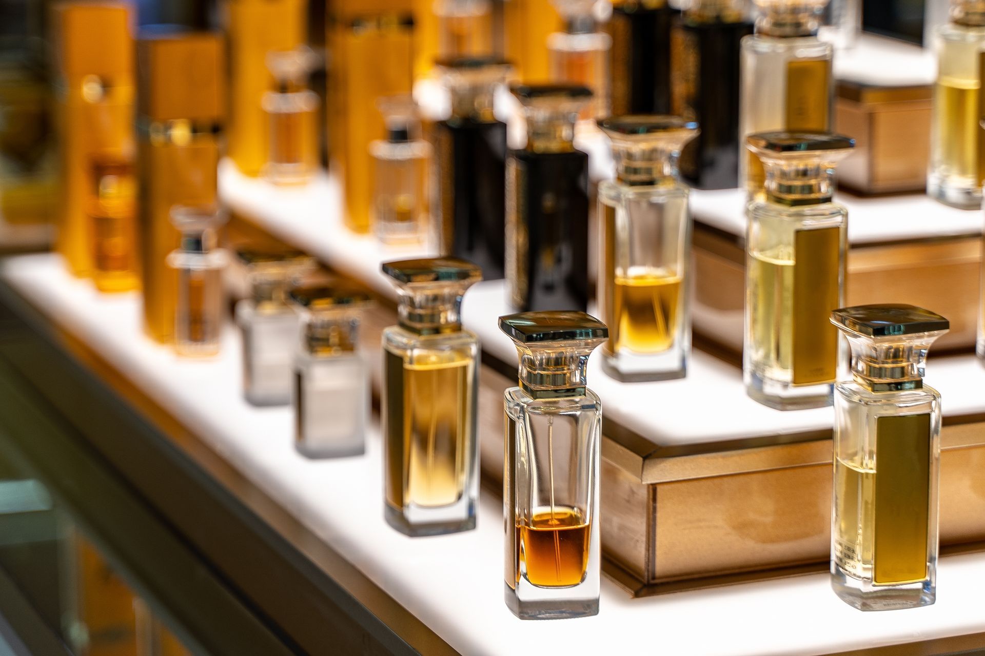 Des rangées de flacons de parfum de différentes nuances sur une étagère de présentation à plusieurs niveaux.