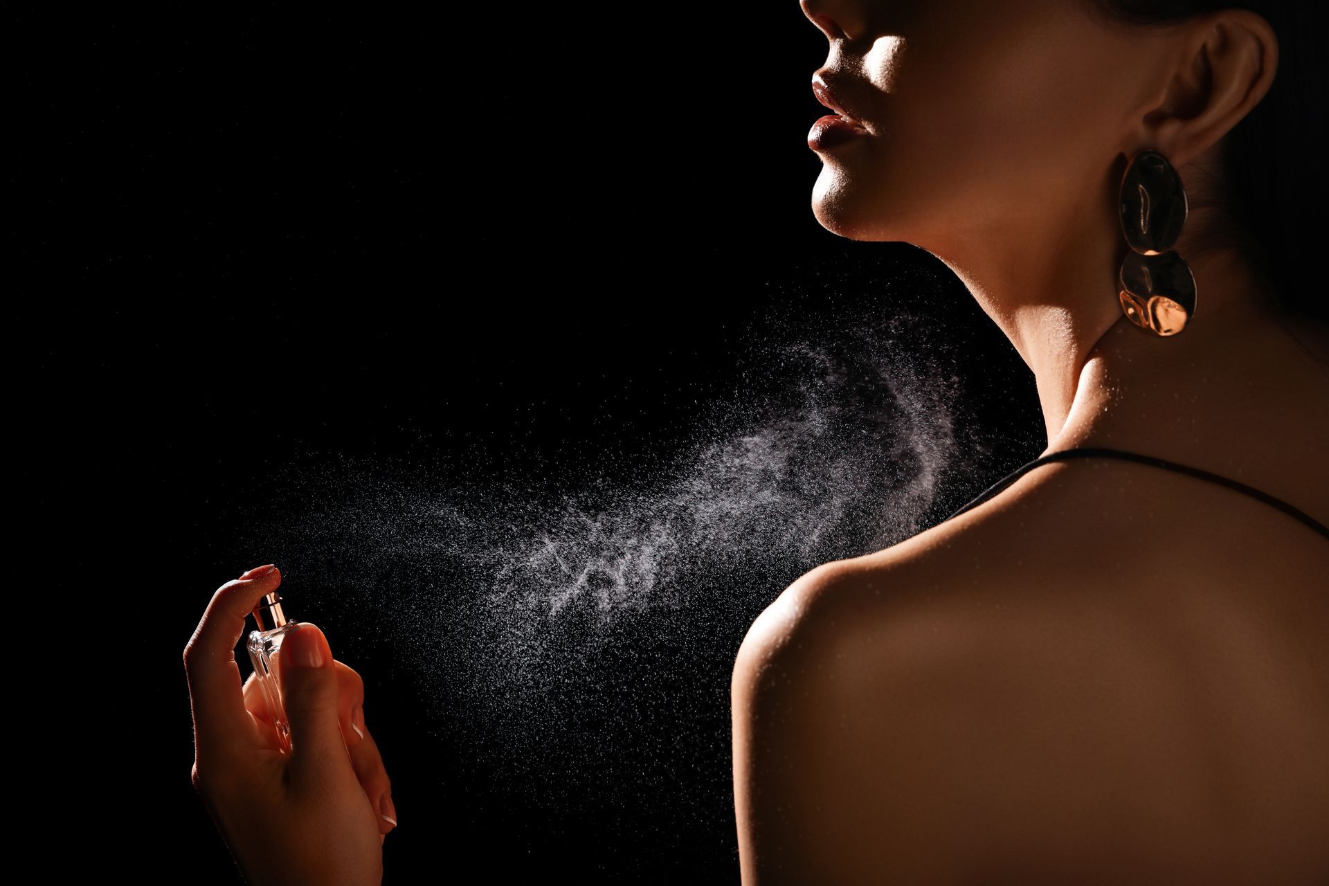 Femme vaporisant du parfum sur son épaule, sur fond noir.