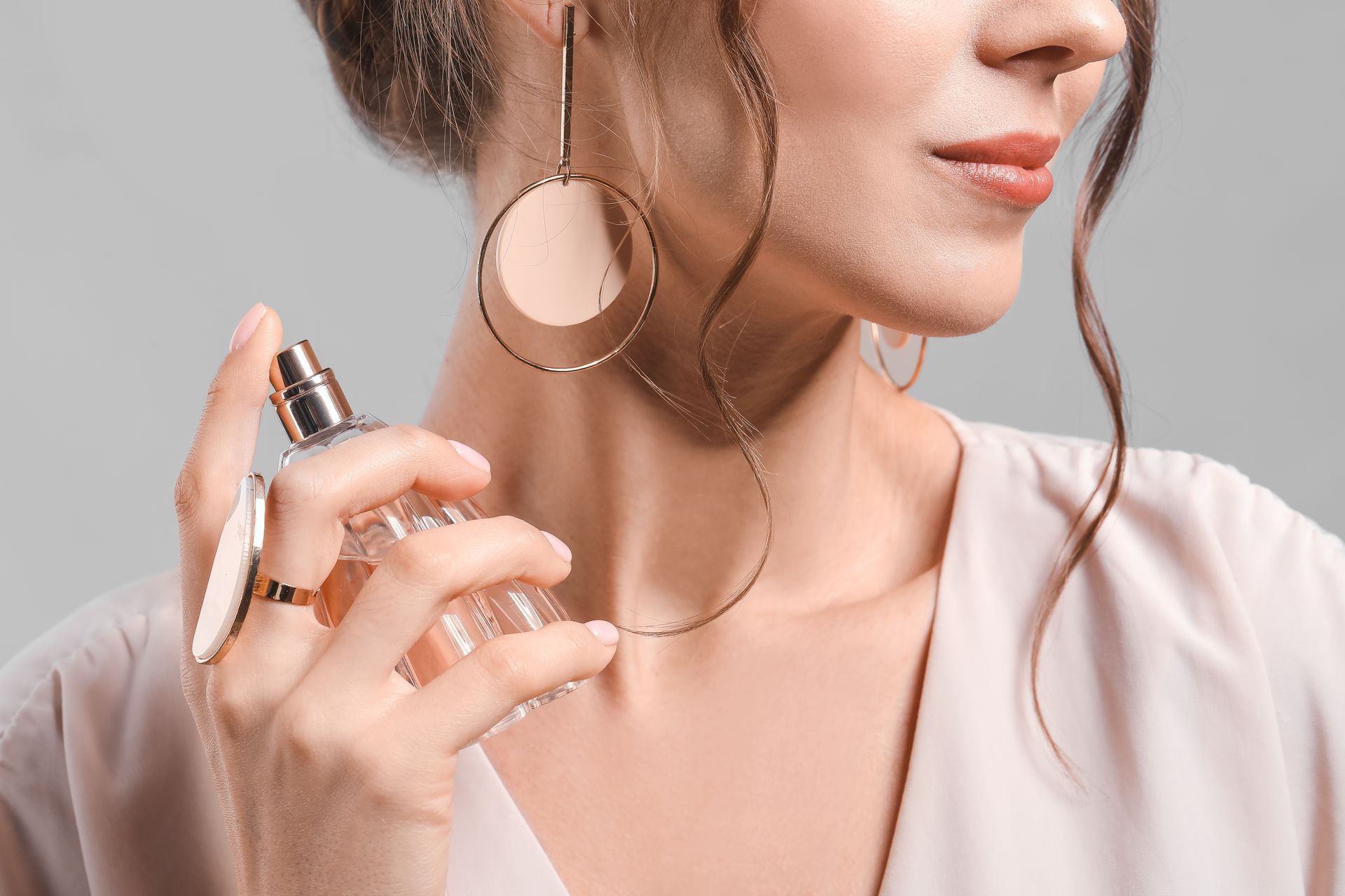 Femme vaporisant du parfum sur son cou, portant des boucles d'oreilles et des bagues en or.