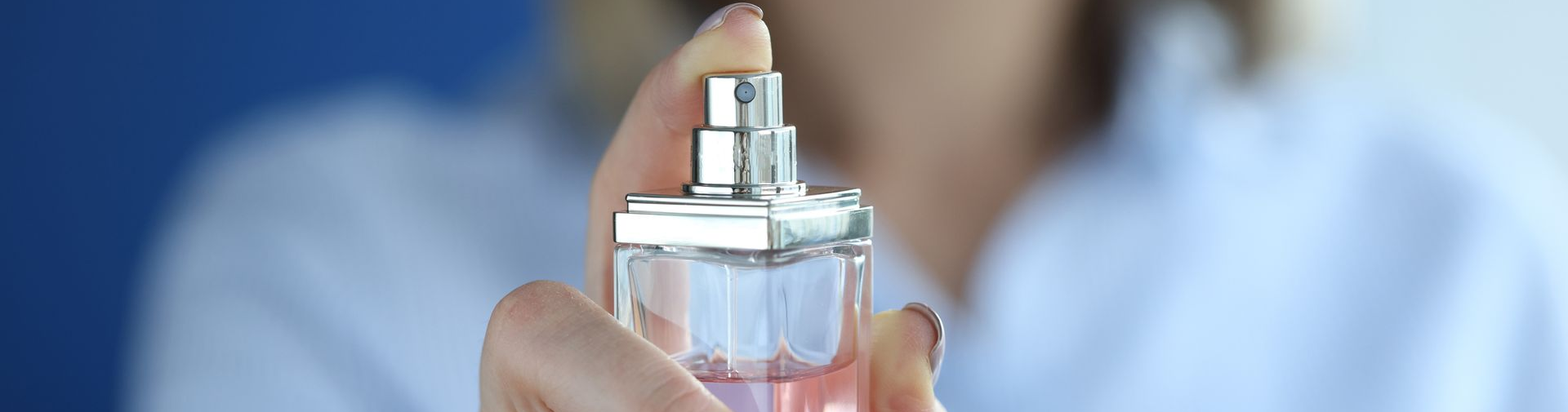 Main de femme tenant un flacon de parfum, prêt à vaporiser. Liquide rose, bouchon argenté.