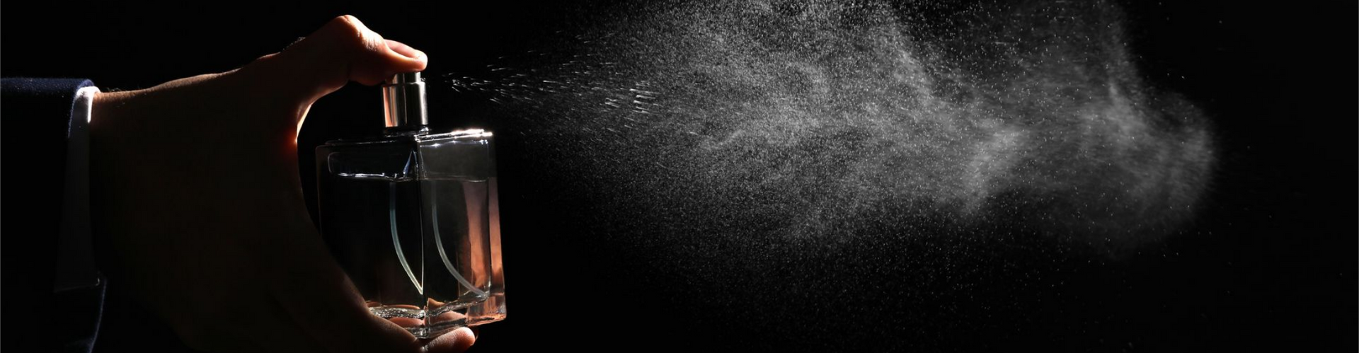 Pulvérisation manuelle de parfum, créant un nuage de brume sur un fond noir.