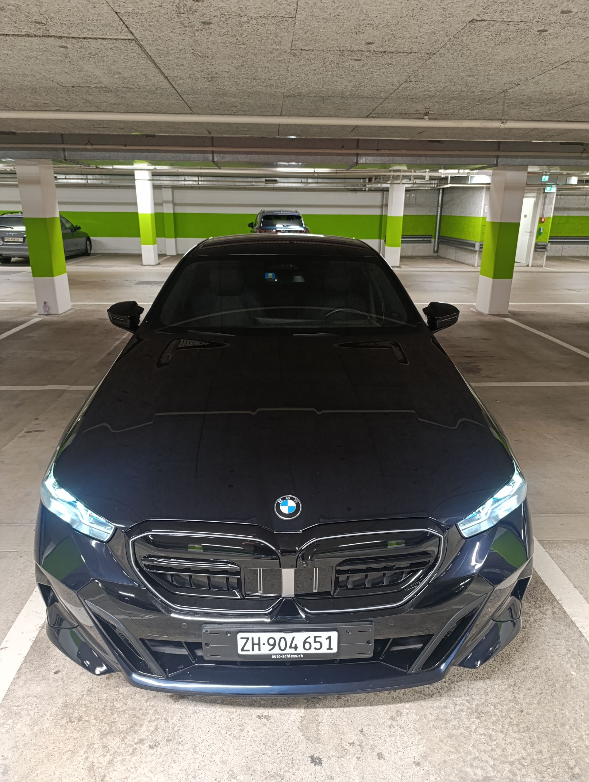 Schwarze BMW Limousine in einer überdachten Garage geparkt, Frontansicht mit eingeschalteten Scheinwerfern.