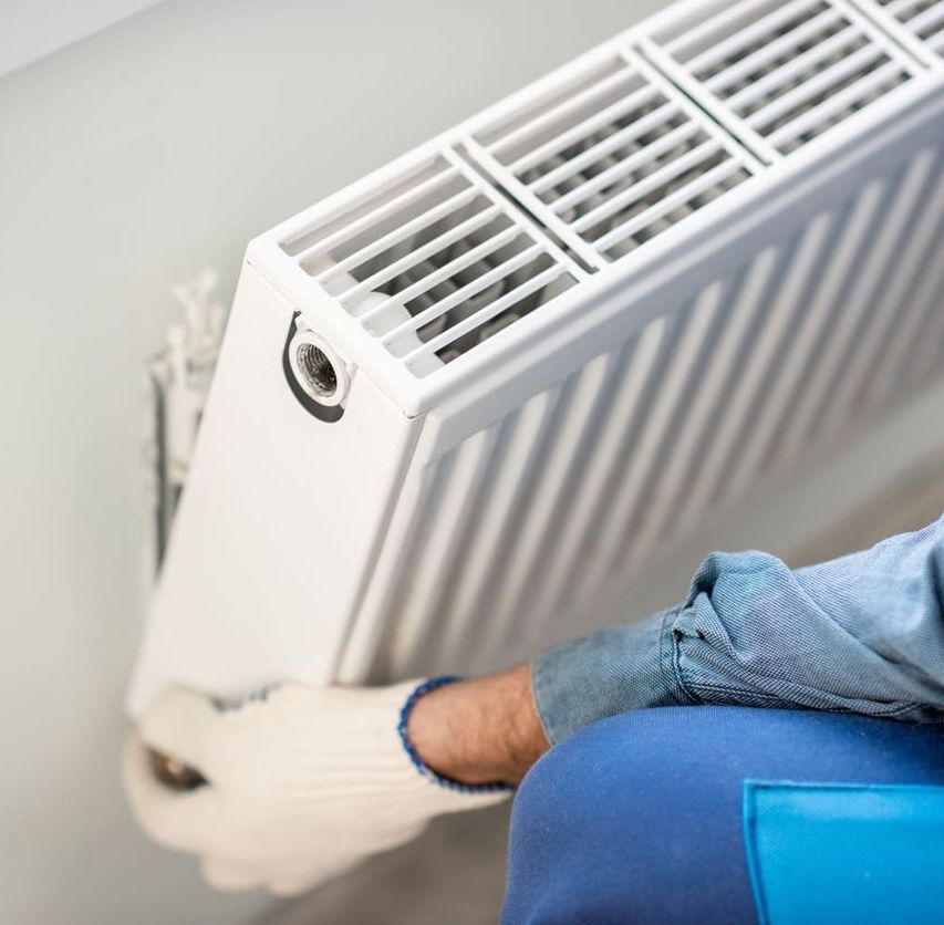 Un hombre está arreglando un radiador en una pared.