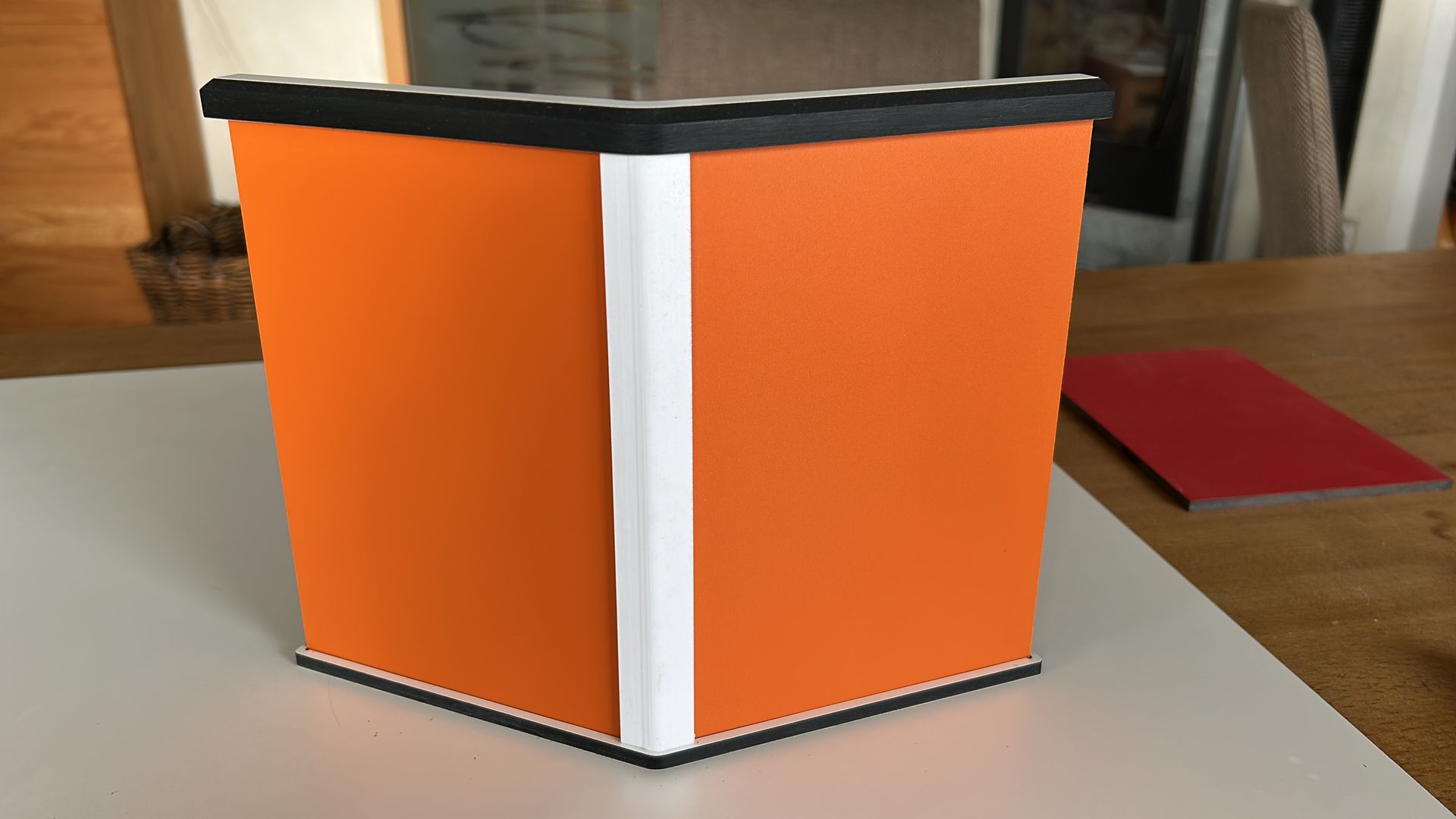 Eine orangefarbene Schachtel steht auf einem Tisch neben einem roten Buch