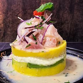 Torre de ceviche: pescado blanco, cebolla roja y cilantro sobre capas de papa amarilla, aguacate y salsa blanca.
