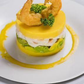 Plato en capas con papa amarilla, aguacate, camarones y salsa; adornado con perejil.