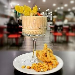 Un cóctel en una copa con tallo y bocadillos fritos en un plato en un restaurante.