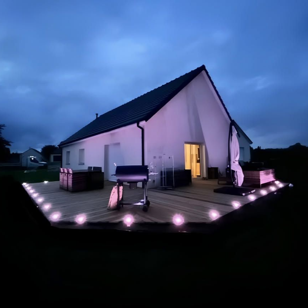 Maison avec des lumières de terrasse allumées au crépuscule, vue depuis un patio à l'arrière.