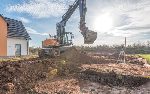 Une pelleteuse creuse la terre à côté d'une maison sur un chantier de construction sous un ciel radieux.