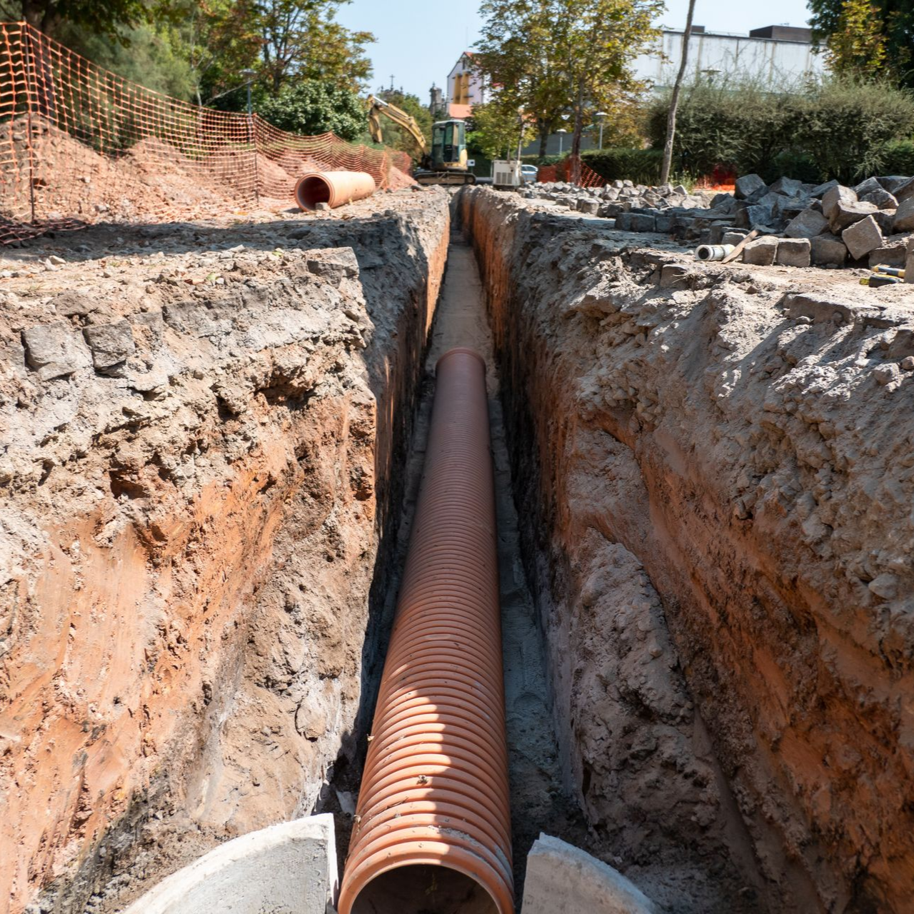 Un tuyau de drainage orange ondulé, posé dans une profonde tranchée de terre sur un chantier de construction.