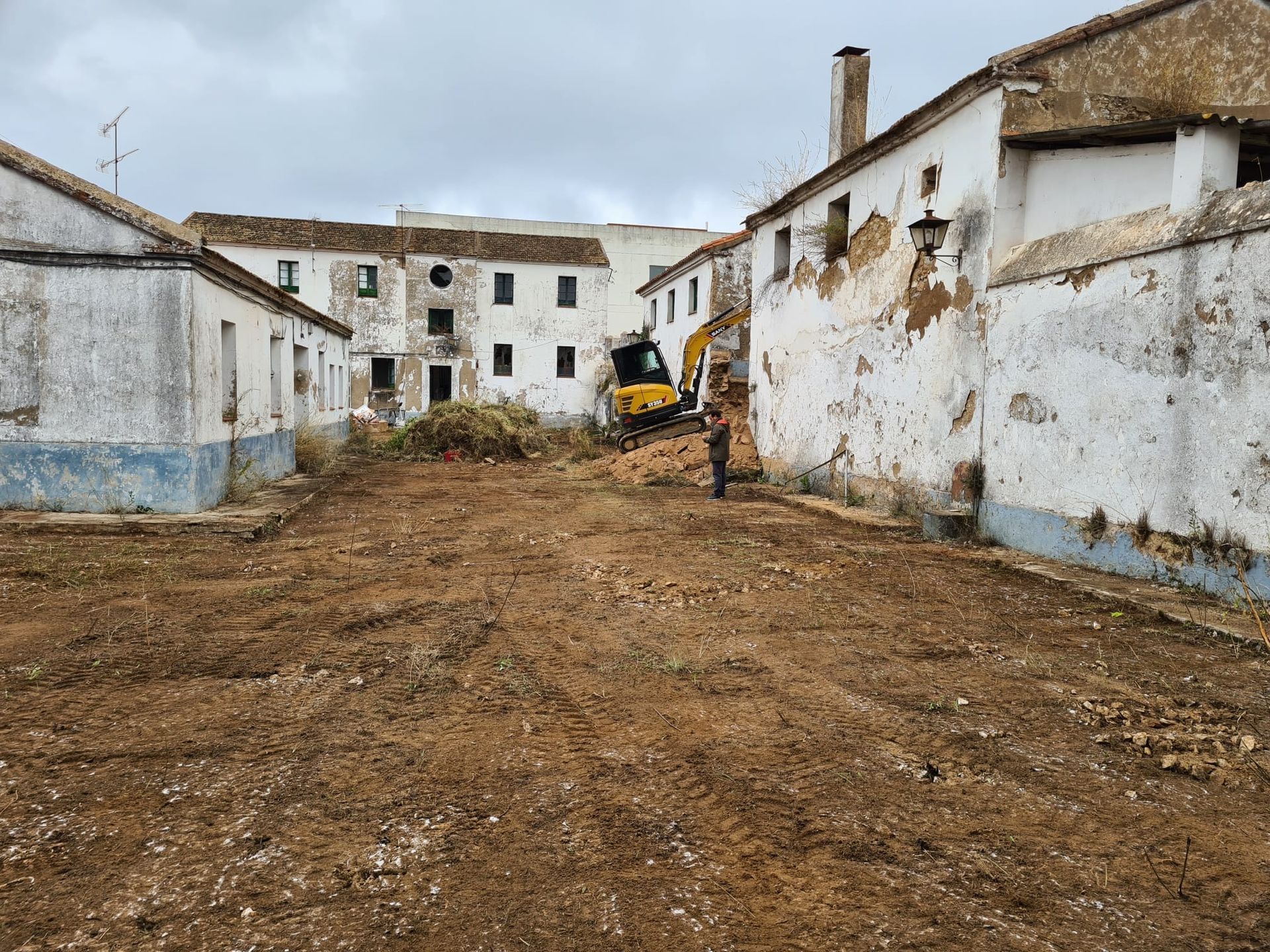 Una excavadora amarilla está moviendo tierra frente a una hilera de edificios blancos.