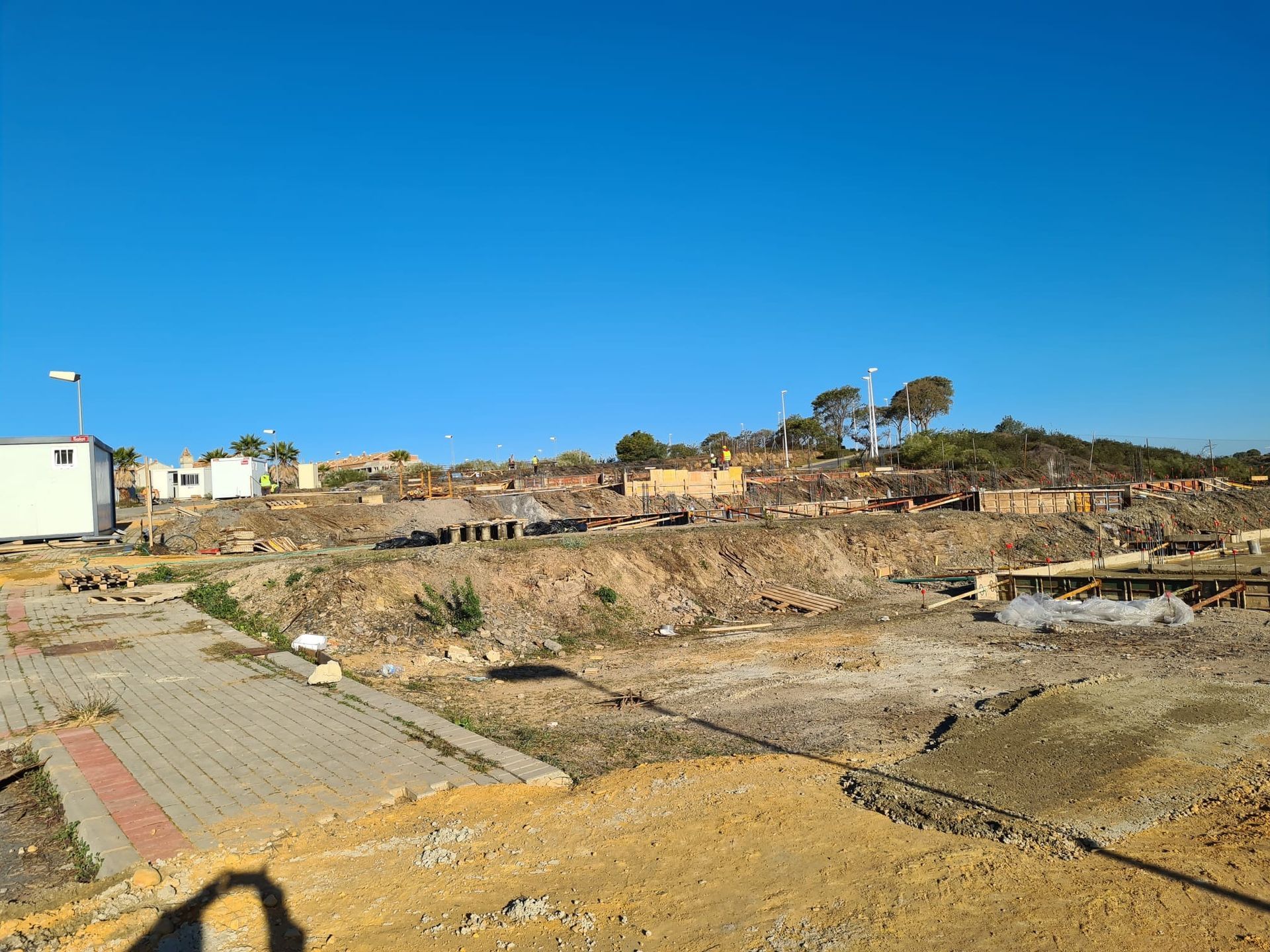 La sombra de una persona se proyecta sobre un campo de tierra con un cielo azul de fondo.