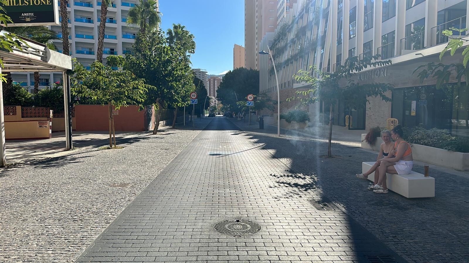 Una pareja está sentada en un banco en una calle adoquinada.