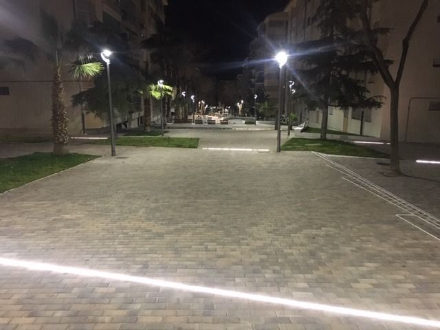 Una pasarela de ladrillos con árboles y farolas por la noche.