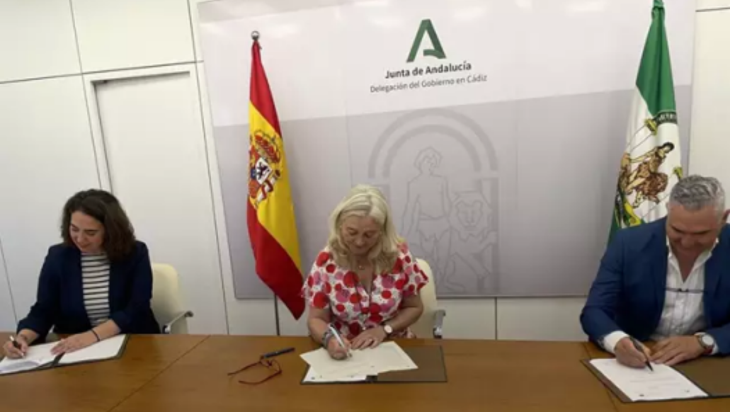 Tres personas están sentadas en una mesa firmando papeles.