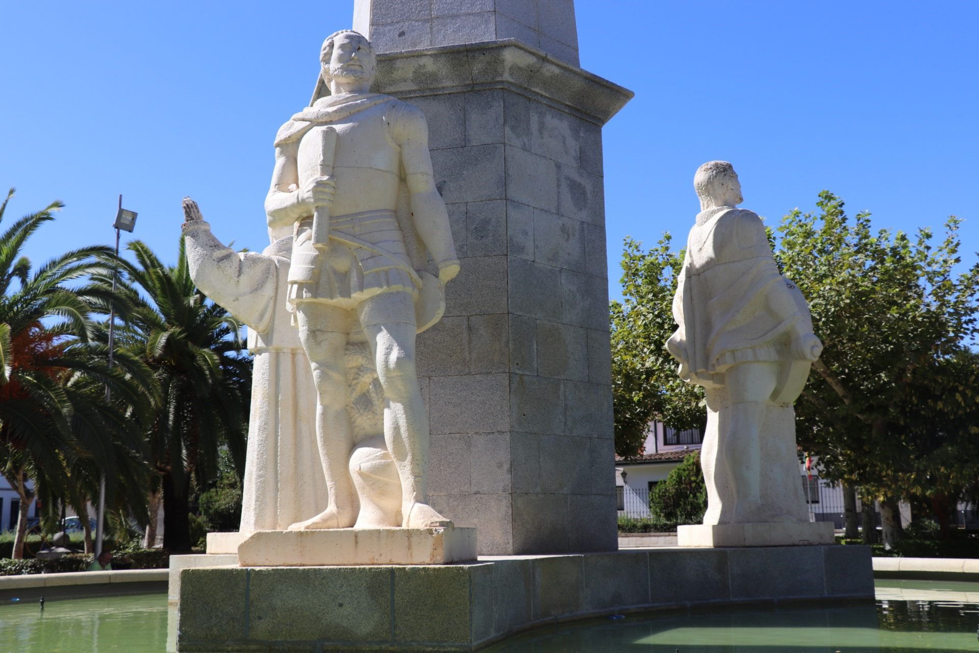Una estatua de un hombre de pie junto a una fuente en un parque.
