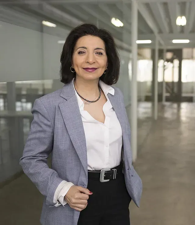 Una mujer que lleva una chaqueta azul y una camisa blanca está parada en un pasillo.