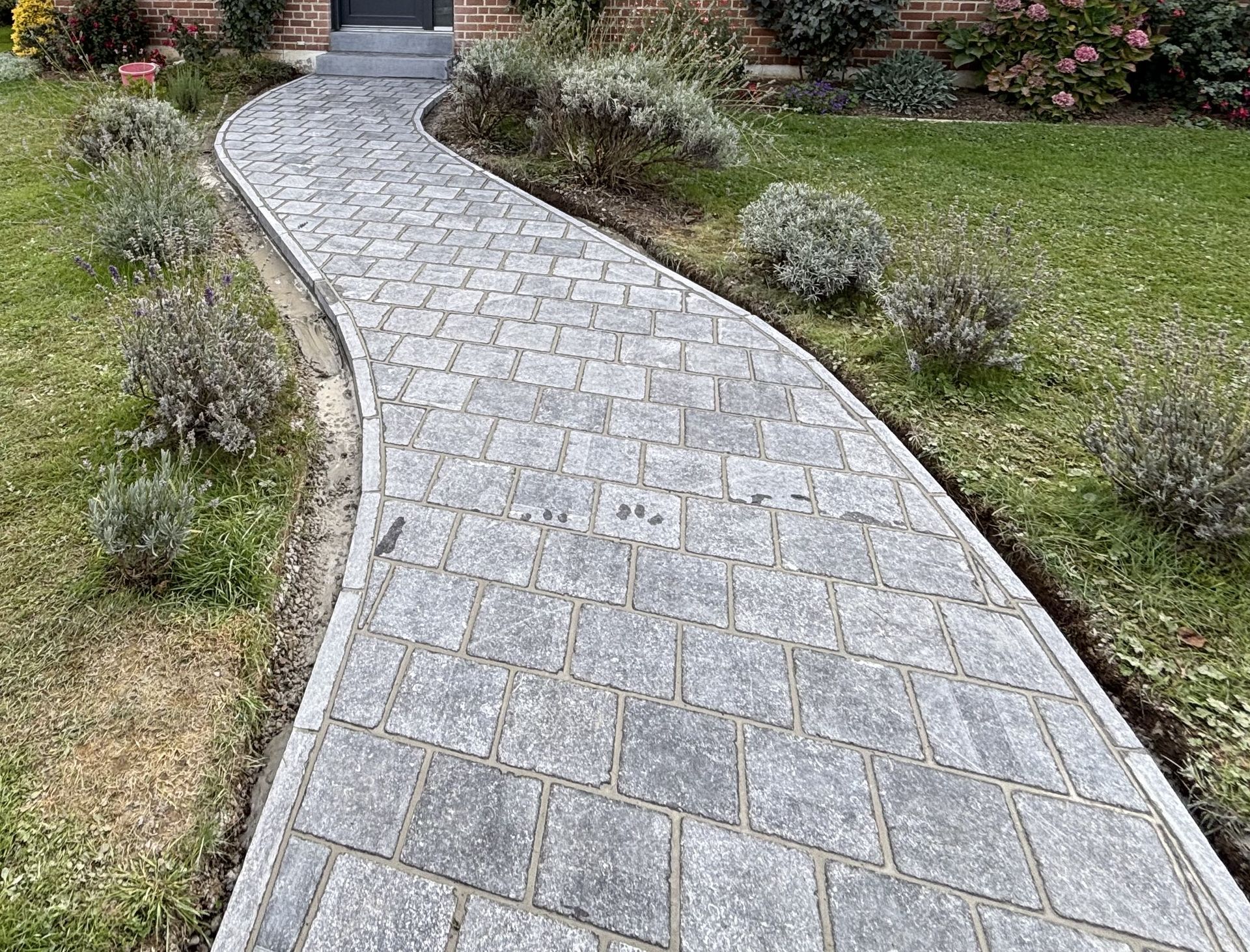 Un chemin de briques serpente à travers une cour herbeuse en direction d'un bâtiment en briques.