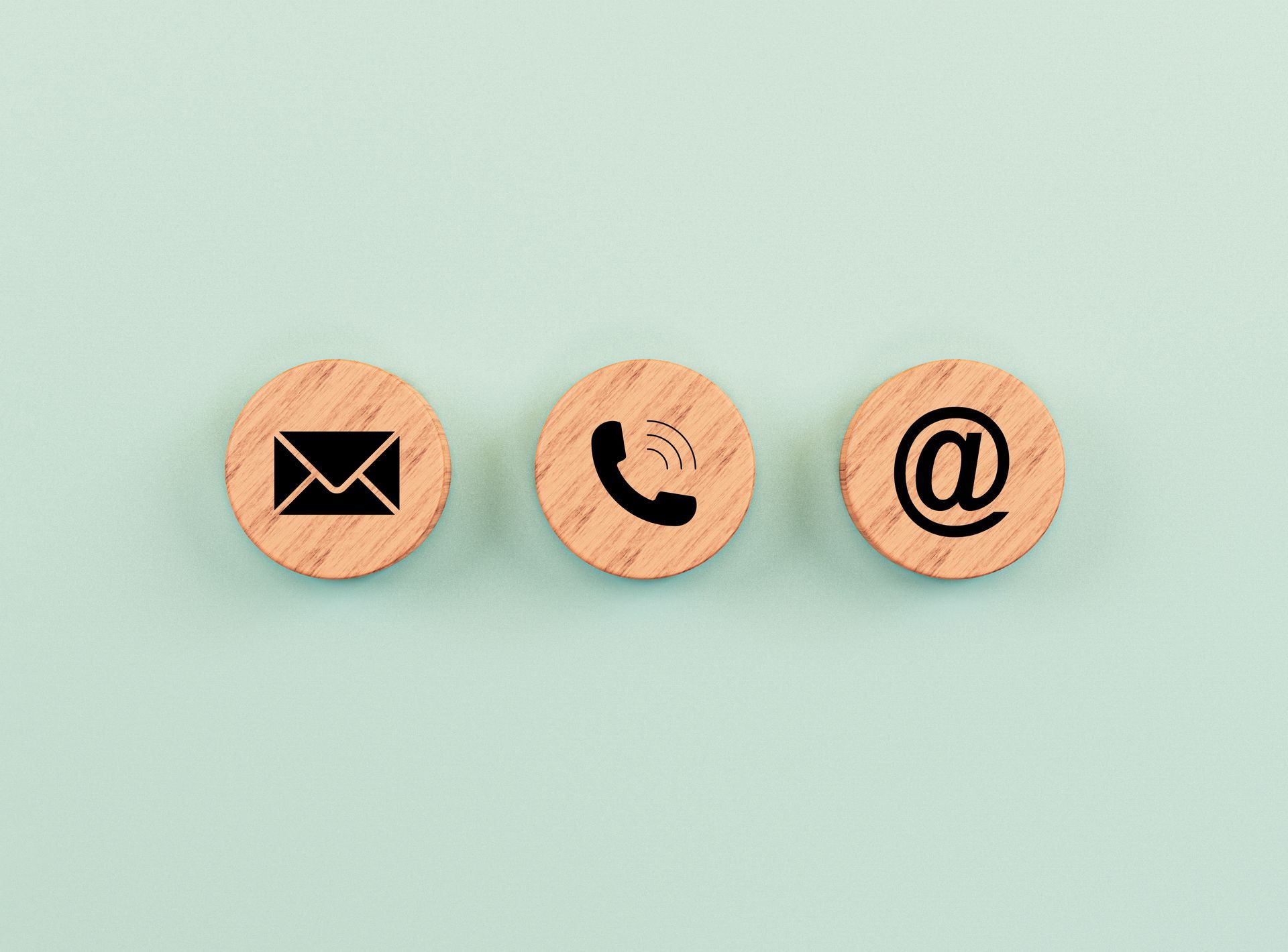 Trois cercles en bois avec des icônes de contact : enveloppe, téléphone et arobase, sur fond bleu clair.