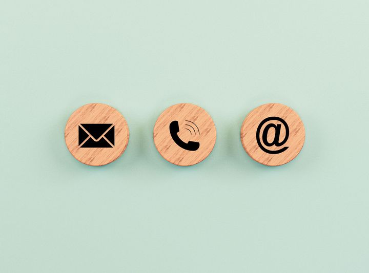 Trois cercles en bois avec des icônes de contact : enveloppe, téléphone et arobase, sur fond bleu clair.