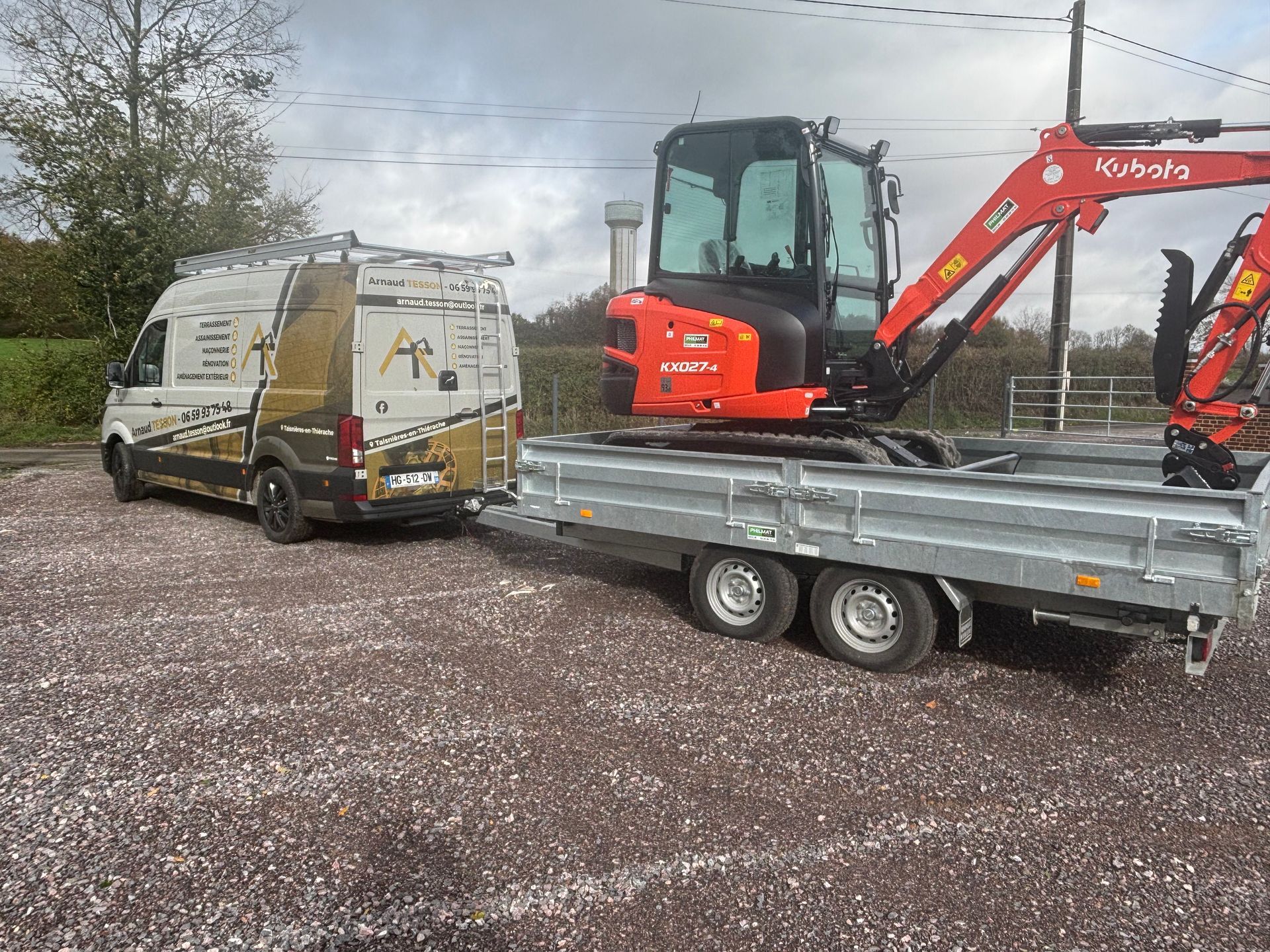 Une camionnette tractant une remorque avec une pelle mécanique Kubota sur un terrain gravillonné.