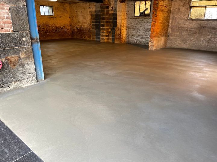 Sol en béton fraîchement coulé avec murs en briques et en pierres apparentes.